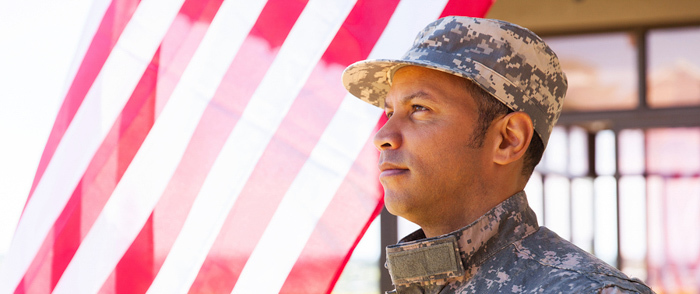 A man in military clothing stands near an American flag