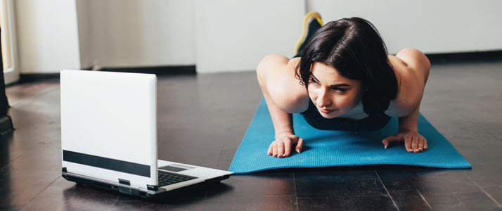woman at home on exercise mat watching video on laptop