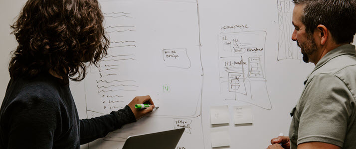 Two colleagues collaborate in front of a white board