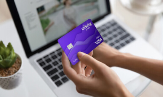 A person holding a purple Wisely paycard in front of a laptop with a website displayed