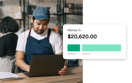 A café worker in an apron using a laptop with an overlay showing Money In: $20,620.00.