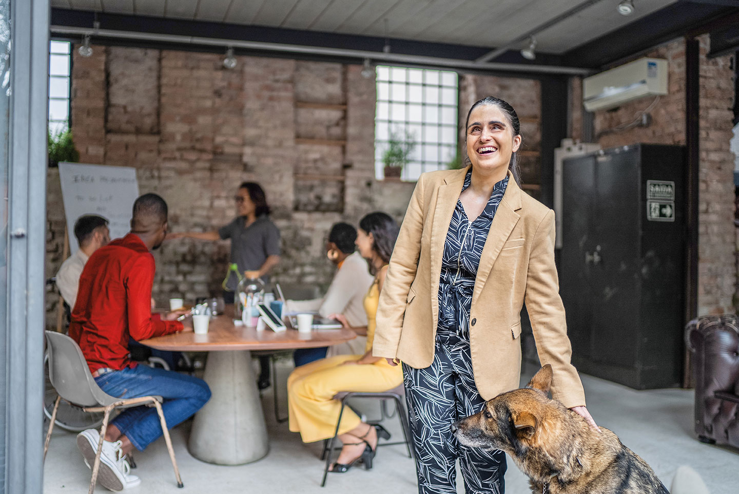 A smiling blind business person with their guide dog in an office.