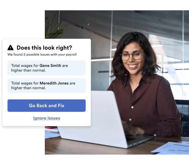 Woman working at a laptop sees a payroll alert about potential high wages for employees, with buttons to Go Back and Fix or Ignore Issues