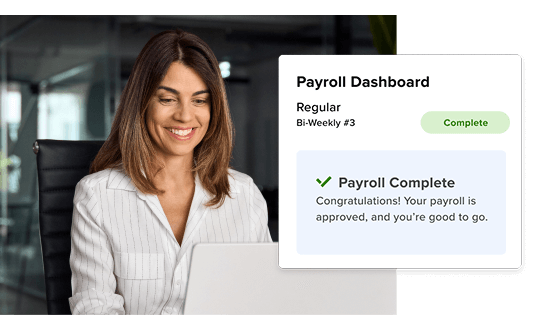 A smiling businesswoman viewing a desktop computer screen with a 'Payroll Complete' notification